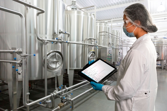 Mujer de pie en la planta de producción de alimentos y bebidas y comprobando el estado de Netilion Asset Health